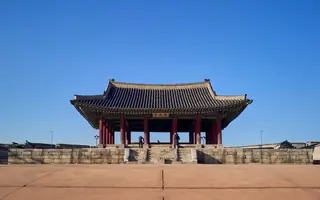 맑은 하늘 아래 서 있는 한국 전통 목조 누각과 돌 기단